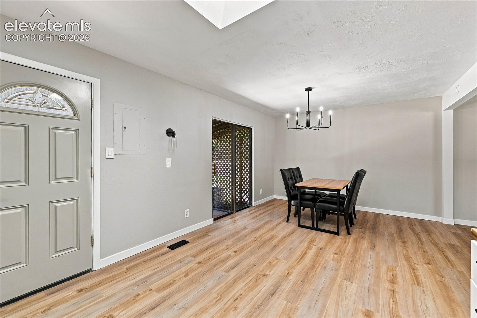 Wood-finish flooring throughout, featuring a contemporary chandelier, a front entry door with an arched decorative glass insert, and sliding glass doors