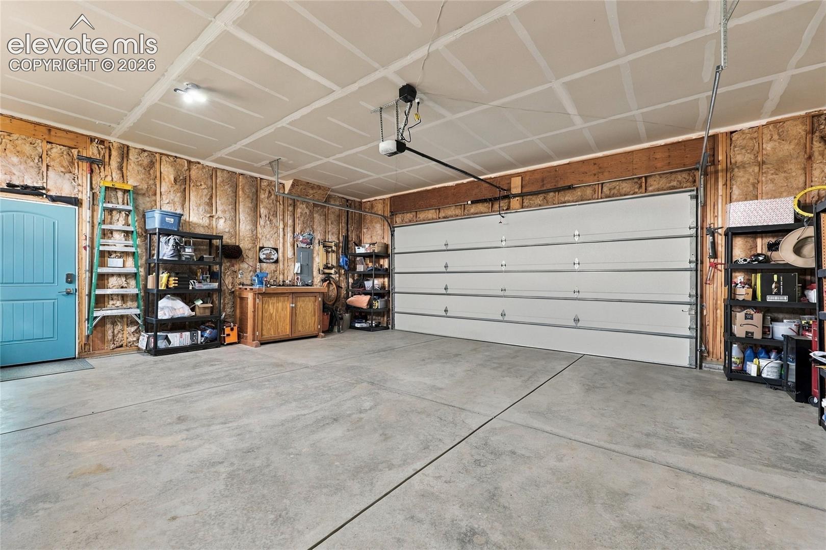 Multi-vehicle garage with concrete flooring, automatic sectional garage door, exposed insulation wall finish, and an attached entry door