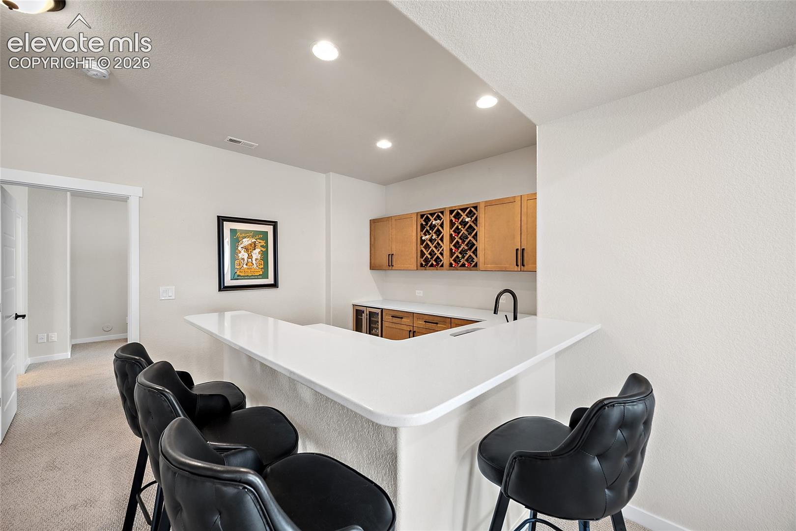 Built-in wet bar featuring a white countertop, wood cabinetry, integrated wine storage, and a sink with a matte black faucet