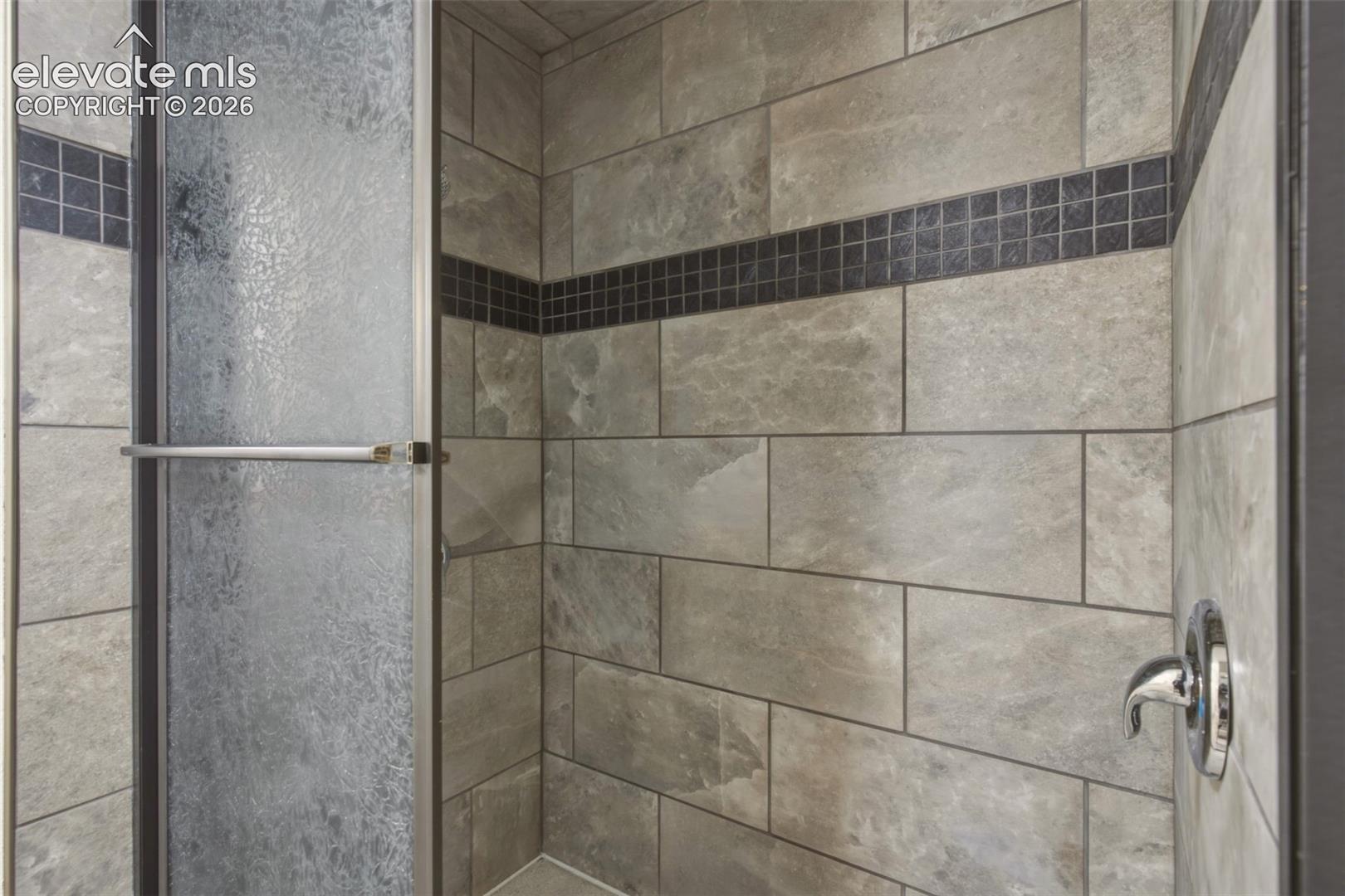 Walk-in shower with textured glass enclosure, tiled walls, and decorative mosaic accent banding
