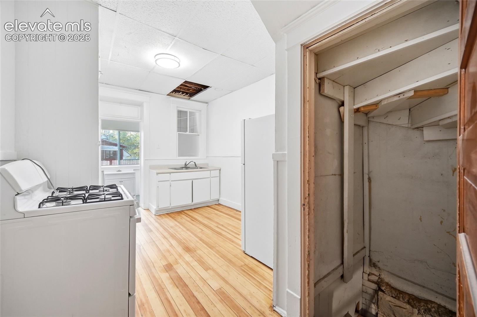 Kitchen area featuring wood-finish flooring, white cabinetry with a light-toned countertop, a stainless steel sink, and a multi-burner gas range