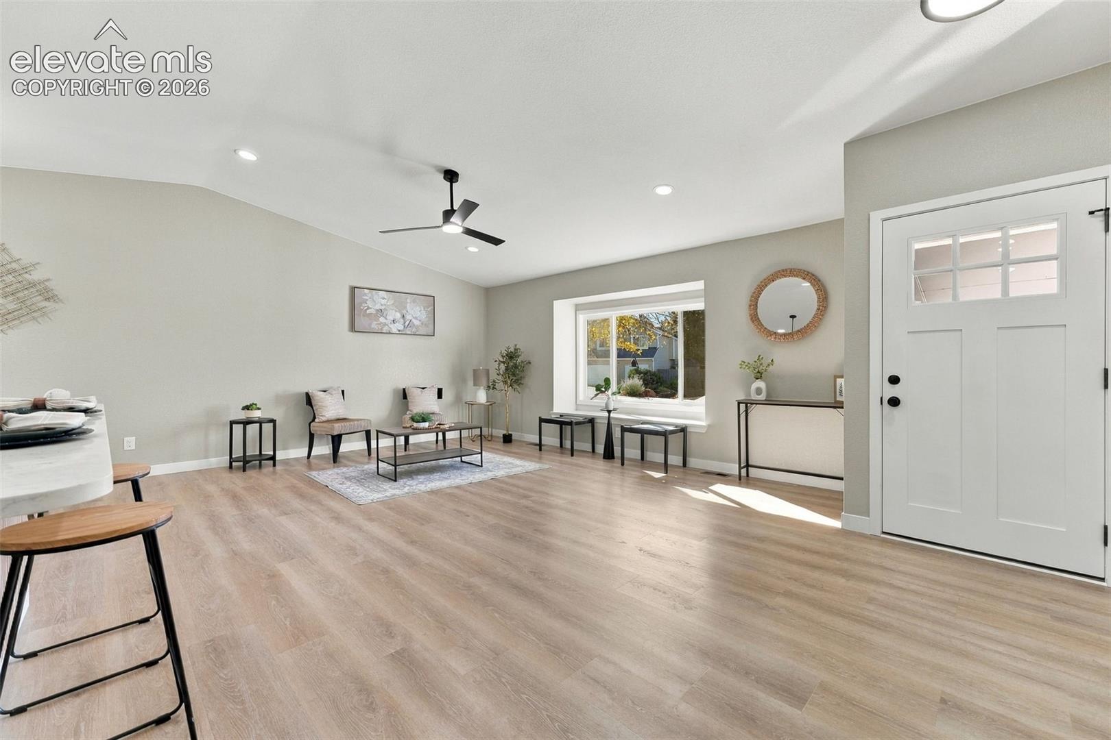 Living area featuring vaulted ceilings, wood-finish flooring, recessed lighting, a ceiling fan, and a picture window