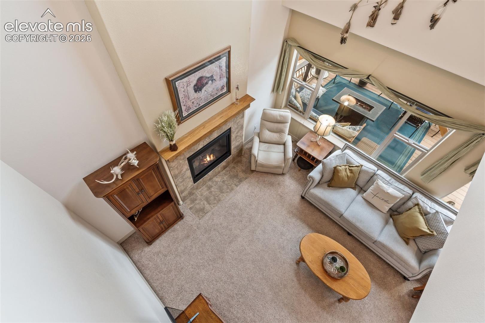 Vaulted living area featuring a stone-faced fireplace with a wood-finish mantel and hearth