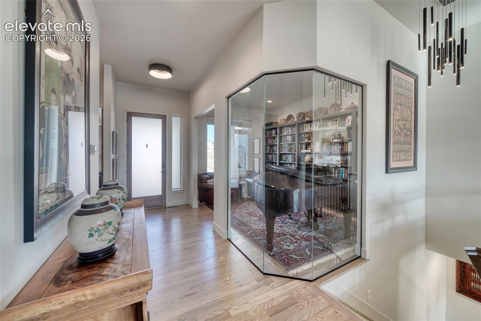 Entryway featuring wood-finish flooring, a glass-enclosed interior room, a frosted-glass panel front door, and modern multi-pendant lighting
