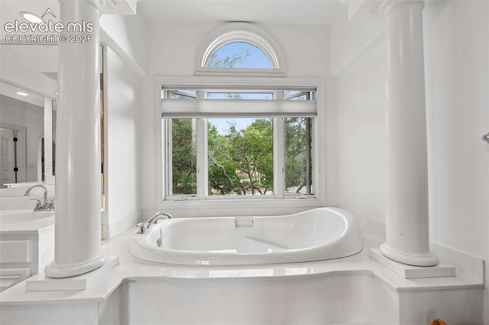 Built-in soaking tub with deck-mounted fixtures, framed by decorative columns