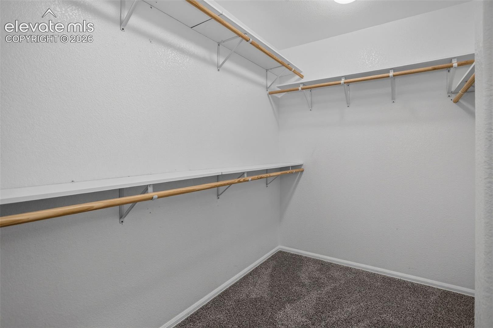 Wall-mounted shelving system with hanging rods, bright white walls, and gray carpet flooring
