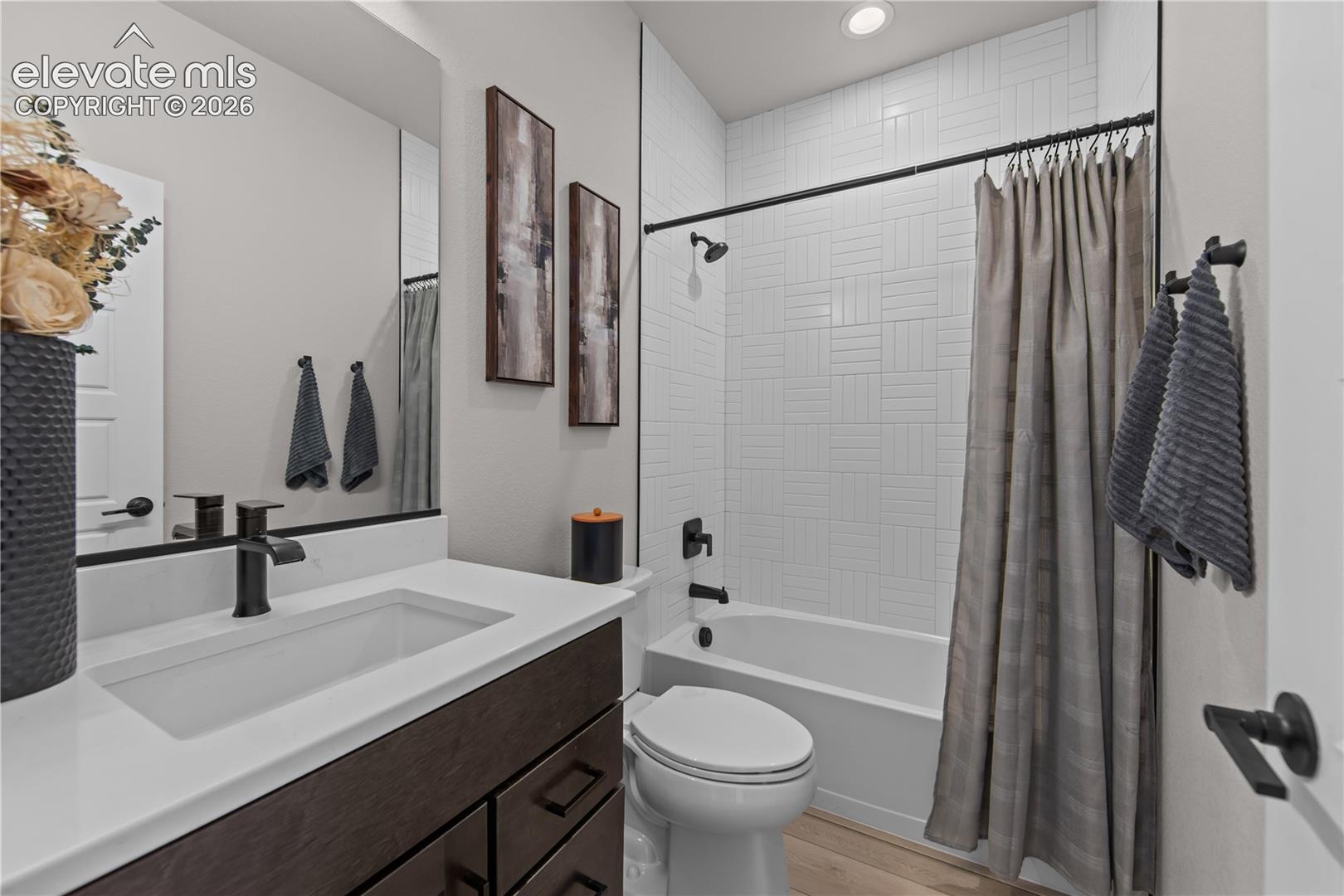 Bathroom featuring a dark wood-finish vanity, a white rectangular undermount sink, a stone-composite countertop, matte black fixtures, and a shower-tub combination with white tile surround
