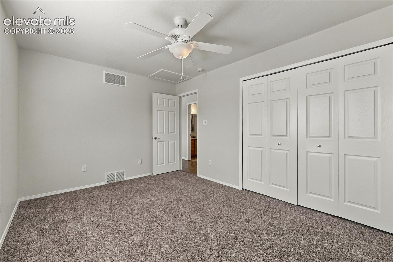 Carpeted room featuring a white ceiling fan with integrated lighting, dual-panel closet doors, and a solid-core interior door