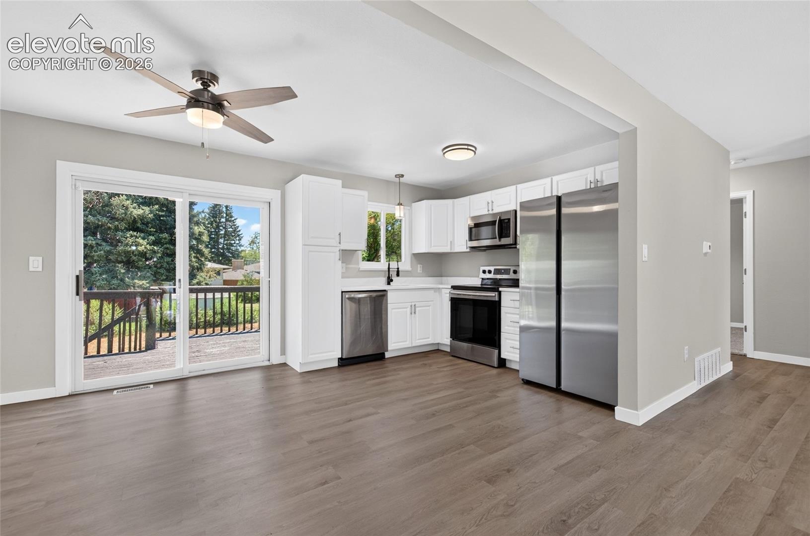 Open-concept living space featuring wood-finish flooring, a ceiling fan with integrated lighting, and a kitchen with white cabinetry and stainless steel appliances