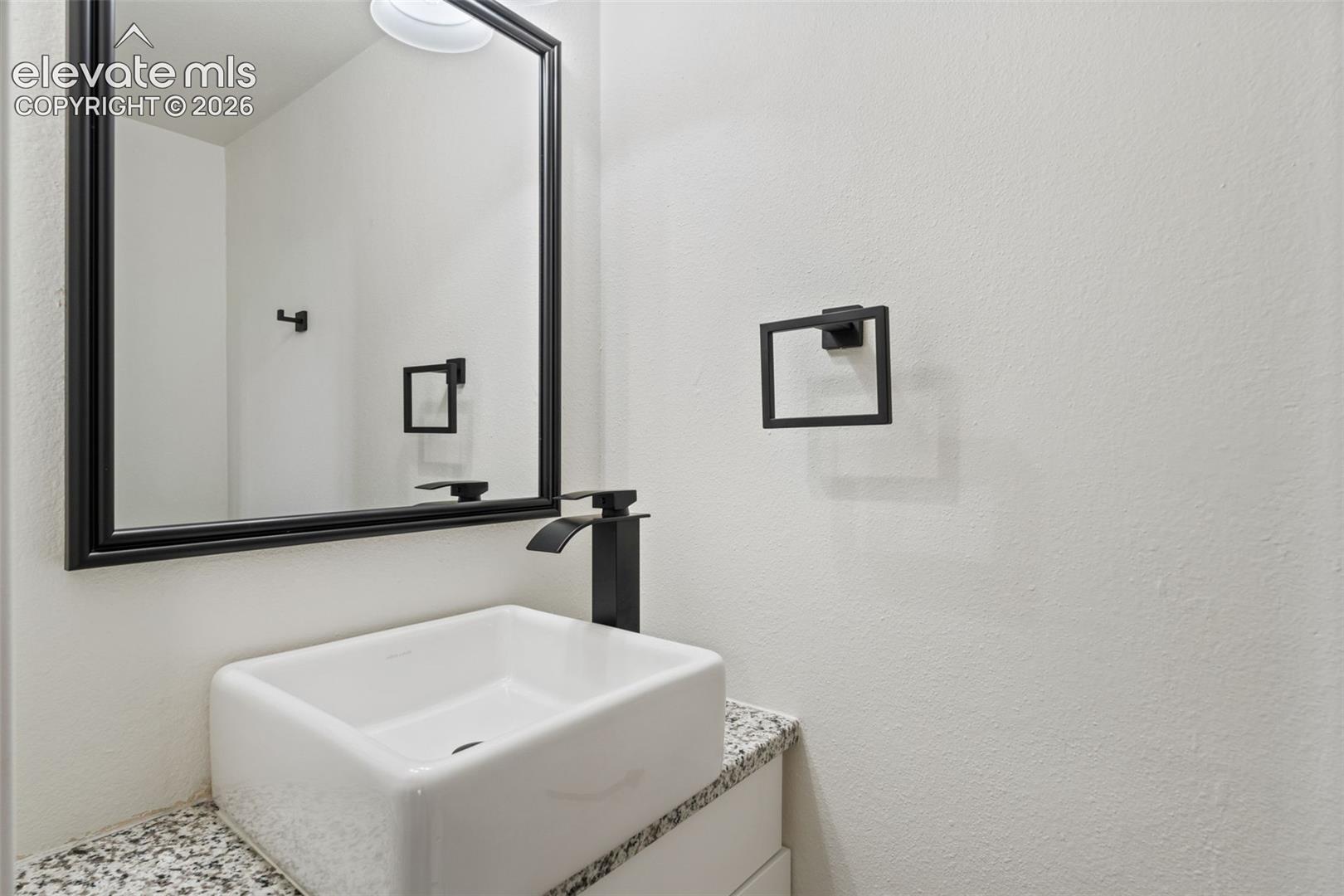 Floating vanity featuring a stone countertop, square vessel sink, matte black faucet, framed mirror, and matching matte black hardware