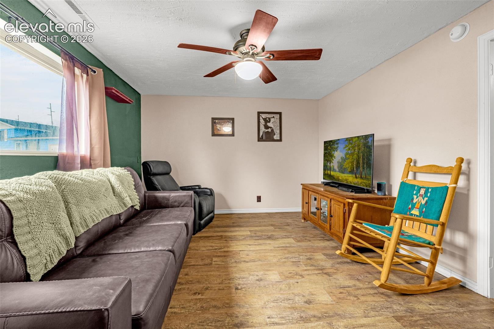 Wood-finish flooring, ceiling fan with integrated lighting, and large window with natural light