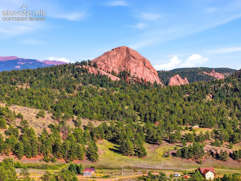 Mountain landscape with a prominent red rock formation, extensive evergreen tree coverage, and distant mountain ranges