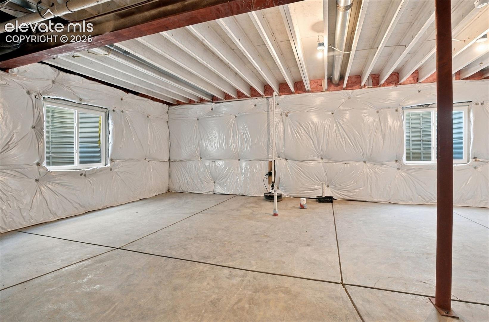 Unfinished lower level featuring concrete flooring, exposed joist ceiling, vapor-barrier wall insulation, and two sliding windows