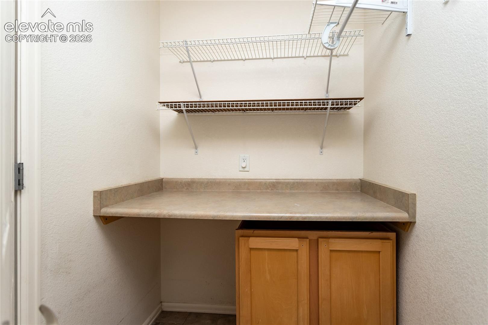 Laundry room with a raised platform for the washer and dryer (not included). Built-in wood cabinetry with a laminate countertop, accompanied by dual-tier wire shelving