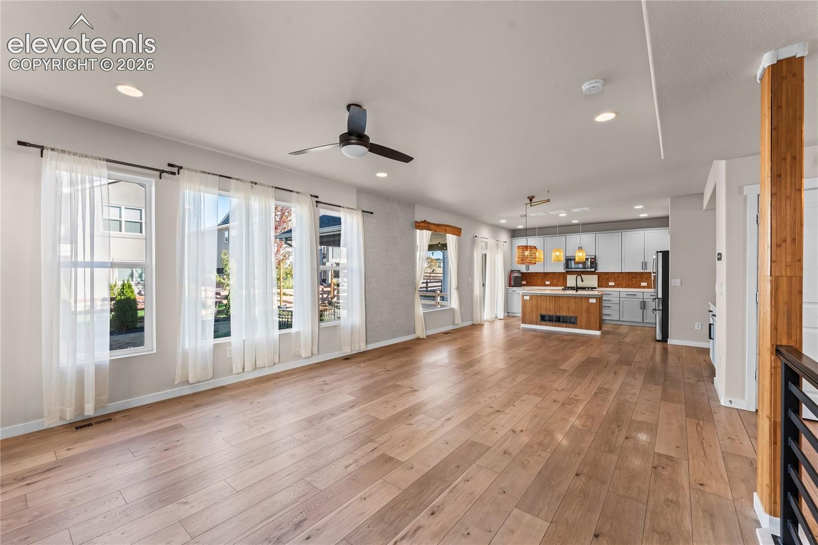 Open-concept interior featuring wood-finish flooring, a kitchen island with wood-tone cabinetry, recessed lighting, and large windows