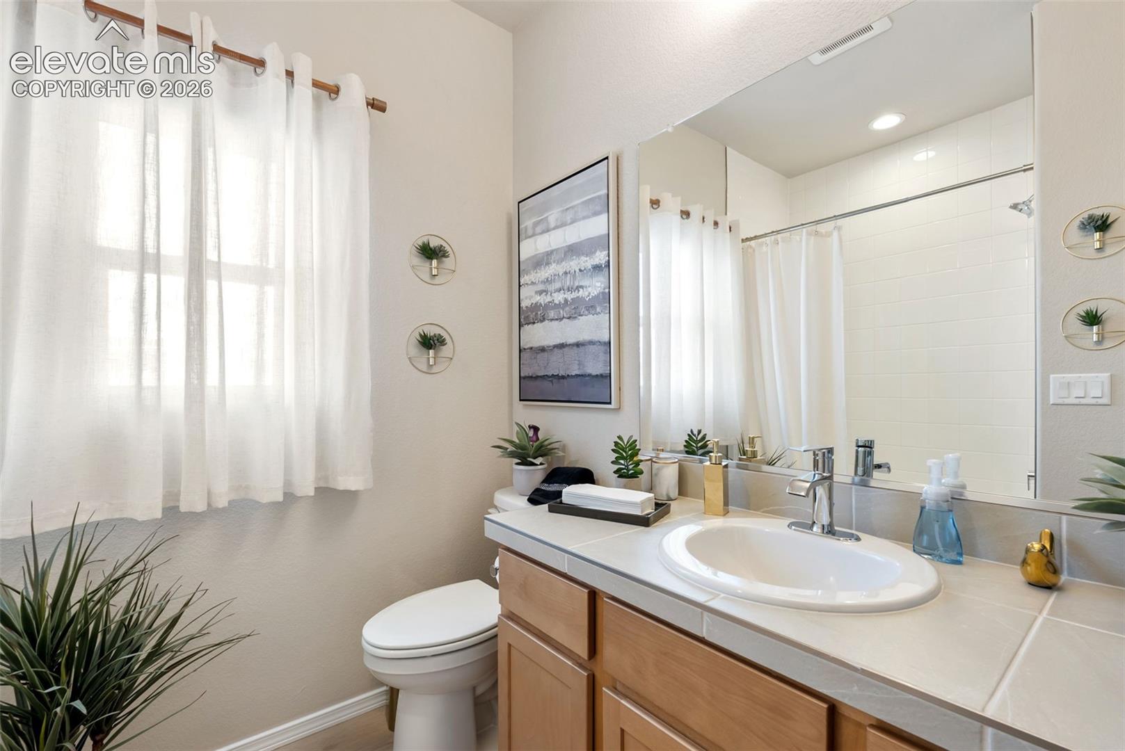 Bathroom vanity featuring tile countertop, oval undermount sink, brushed-metal faucet, and wood-finish cabinetry, complemented by a large wall-mounted mirror