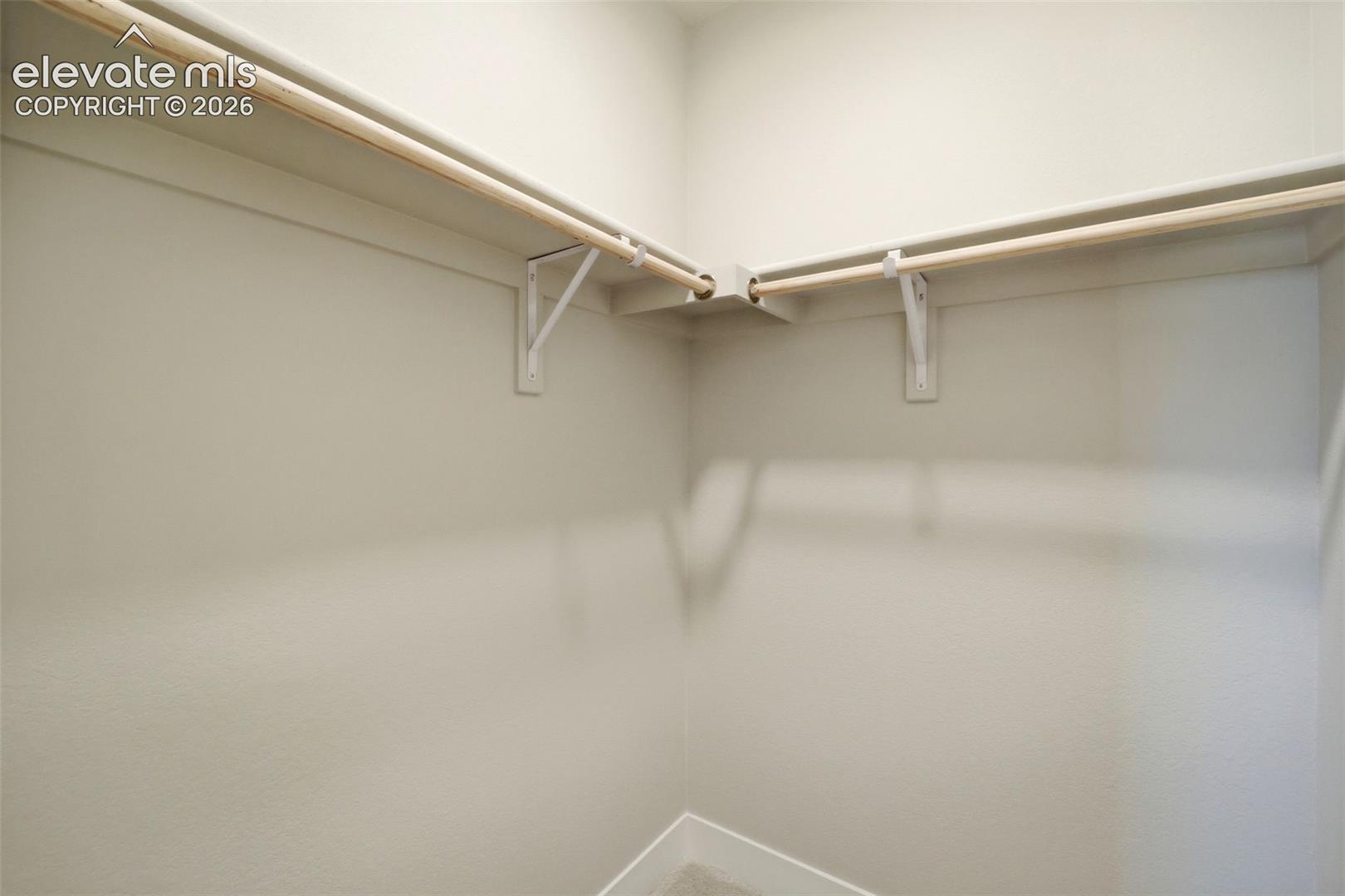 Walk-in closet featuring dual-tier wooden hanging rods, white shelving, and white support brackets