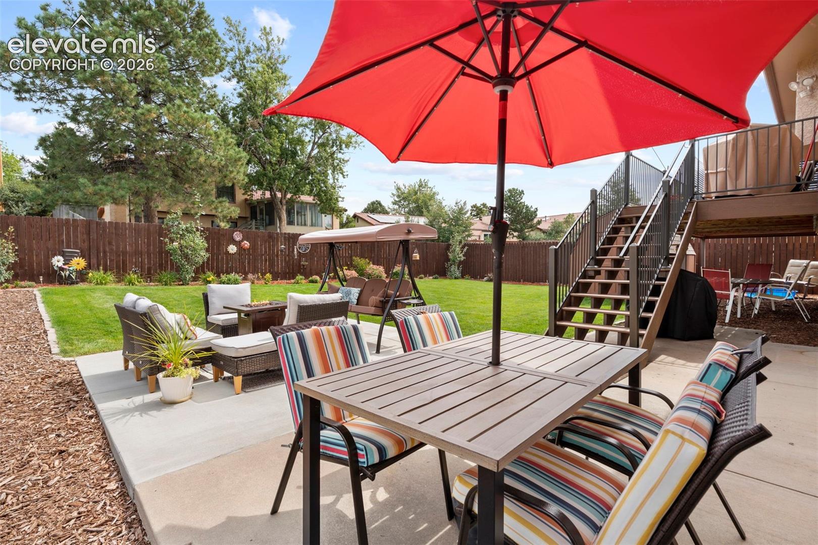 Backyard featuring a concrete patio, wood-finish perimeter fencing, lawn space, and a raised wooden deck with metal railing and stairs