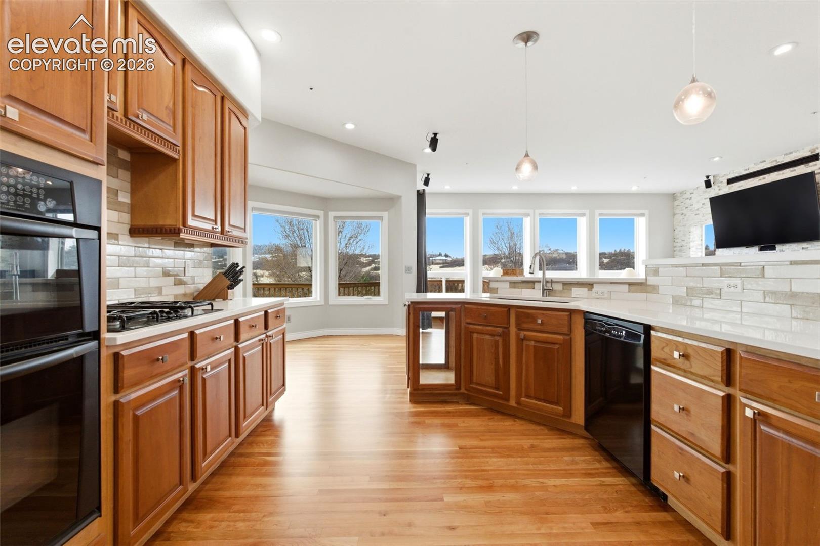 Hardwood flooring throughout, wooden cabinetry, double wall oven, integrated dishwasher, and a tile backsplash