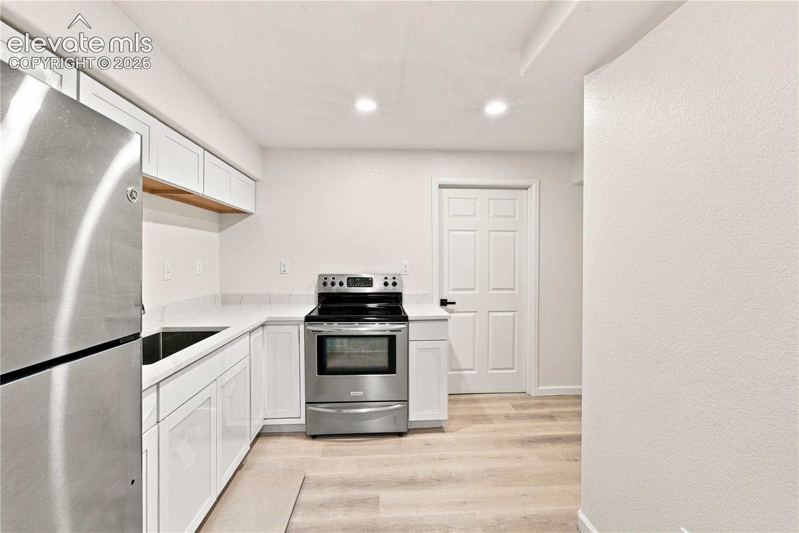 Kitchen featuring white shaker cabinetry, stainless steel appliances, light-toned countertops, and wood-finish flooring
