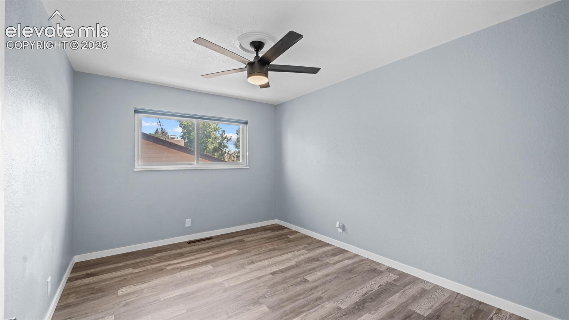 Spacious room featuring wood-finish flooring, light blue walls, and a contemporary ceiling fan with integrated lighting