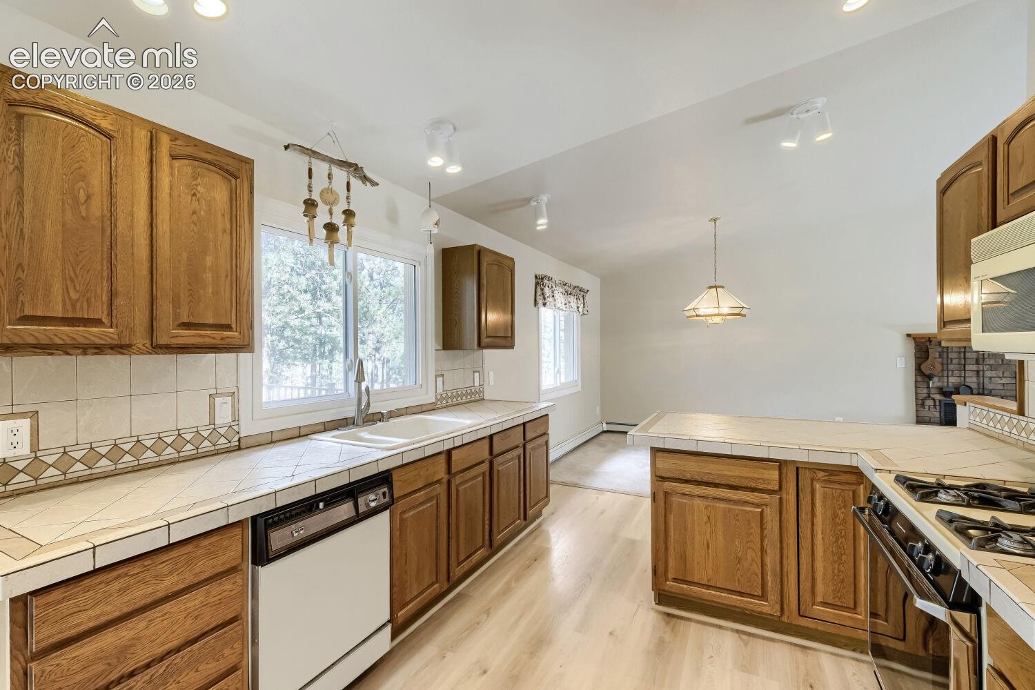 Kitchen featuring wood cabinetry, tile countertops, tile backsplash, and light wood-finish flooring