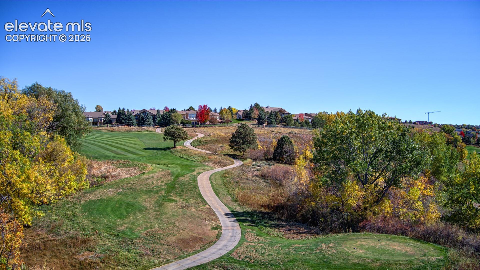 Paved concrete path winding through expansive open space featuring manicured fairways and mature trees