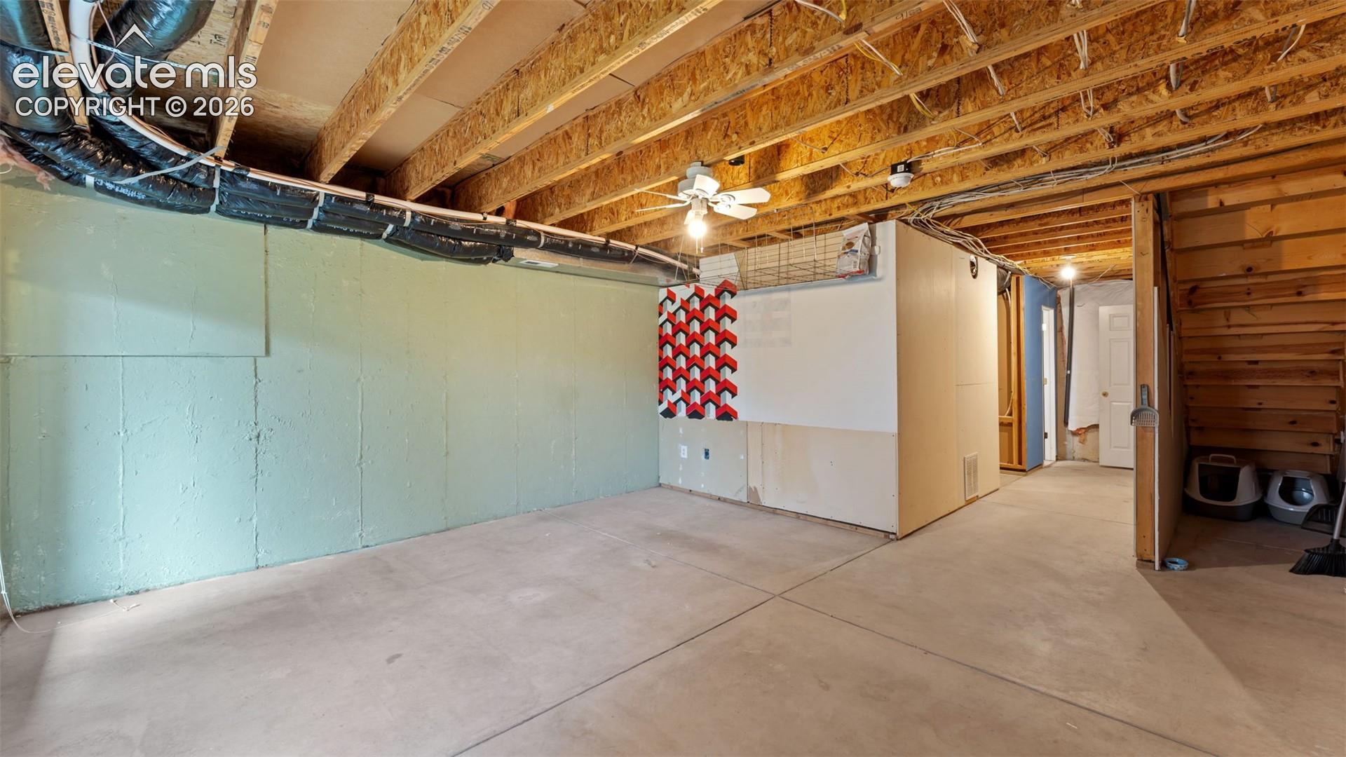 Unfinished lower level featuring exposed wood joist ceilings, concrete flooring, poured concrete walls, and an integrated staircase with wooden steps