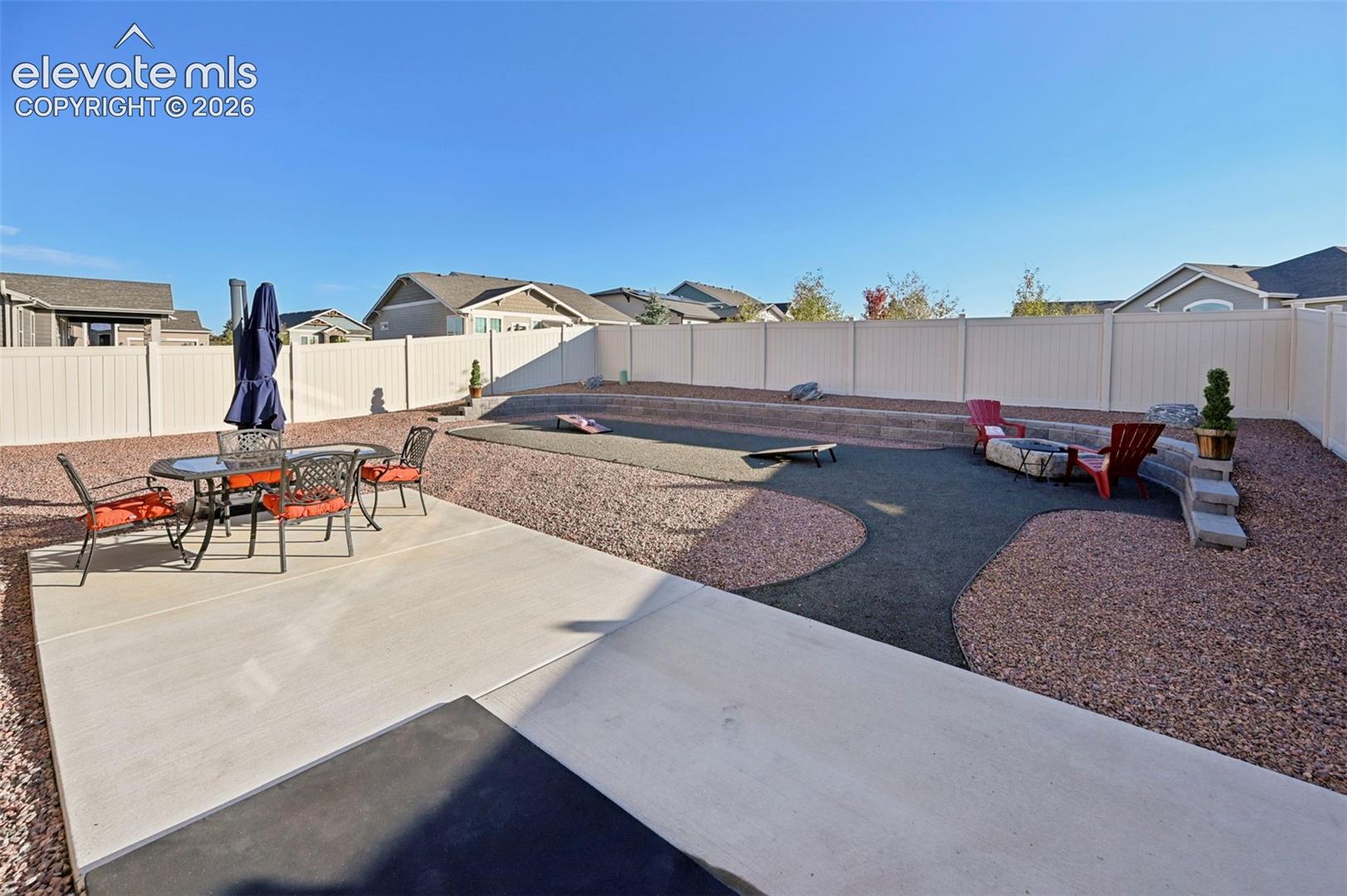 Concrete patio and expansive gravel landscaping featuring a built-in fire pit, privacy fencing, and tiered stone accents