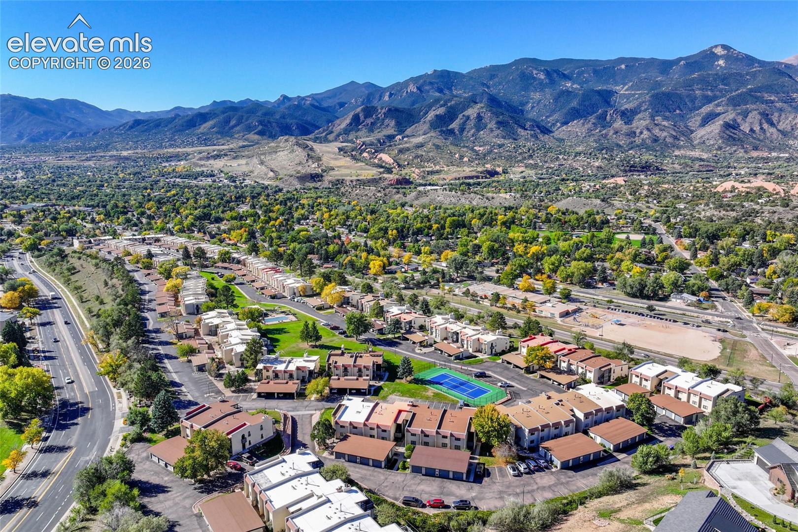 Aerial perspective featuring mountainous topography, mature trees, multi-unit residential structures, and a dedicated tennis court