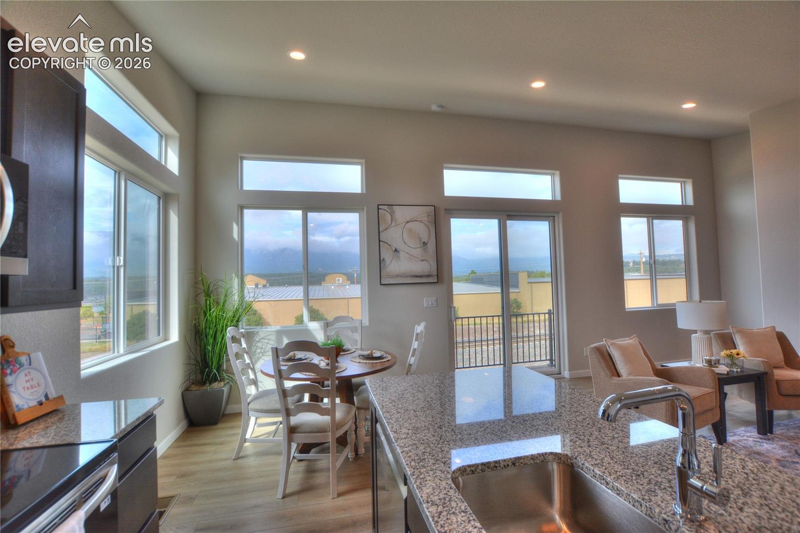 Open-concept living space featuring floor-to-finish wood flooring, granite countertops with integrated sink, stainless steel appliances, and expansive glass doors and windows framing panoramic landscape vistas