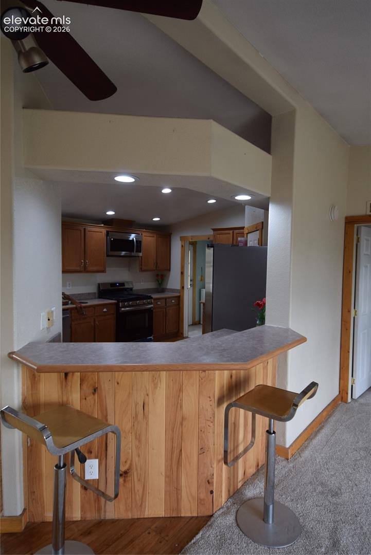 Kitchen pass-through with wood-paneled breakfast bar, recessed lighting, and wood-finish cabinetry