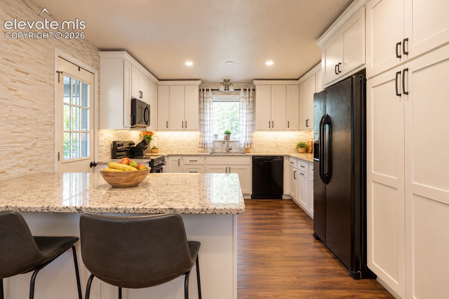 Kitchen featuring granite countertops, white cabinetry, integrated appliances, wood-finish flooring, and a glass-paned door