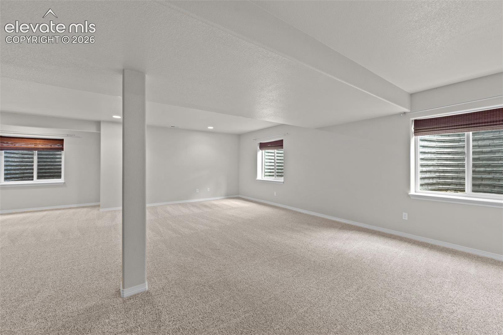 Spacious finished basement with neutral carpet flooring, recessed ceiling lighting, and a structural support column