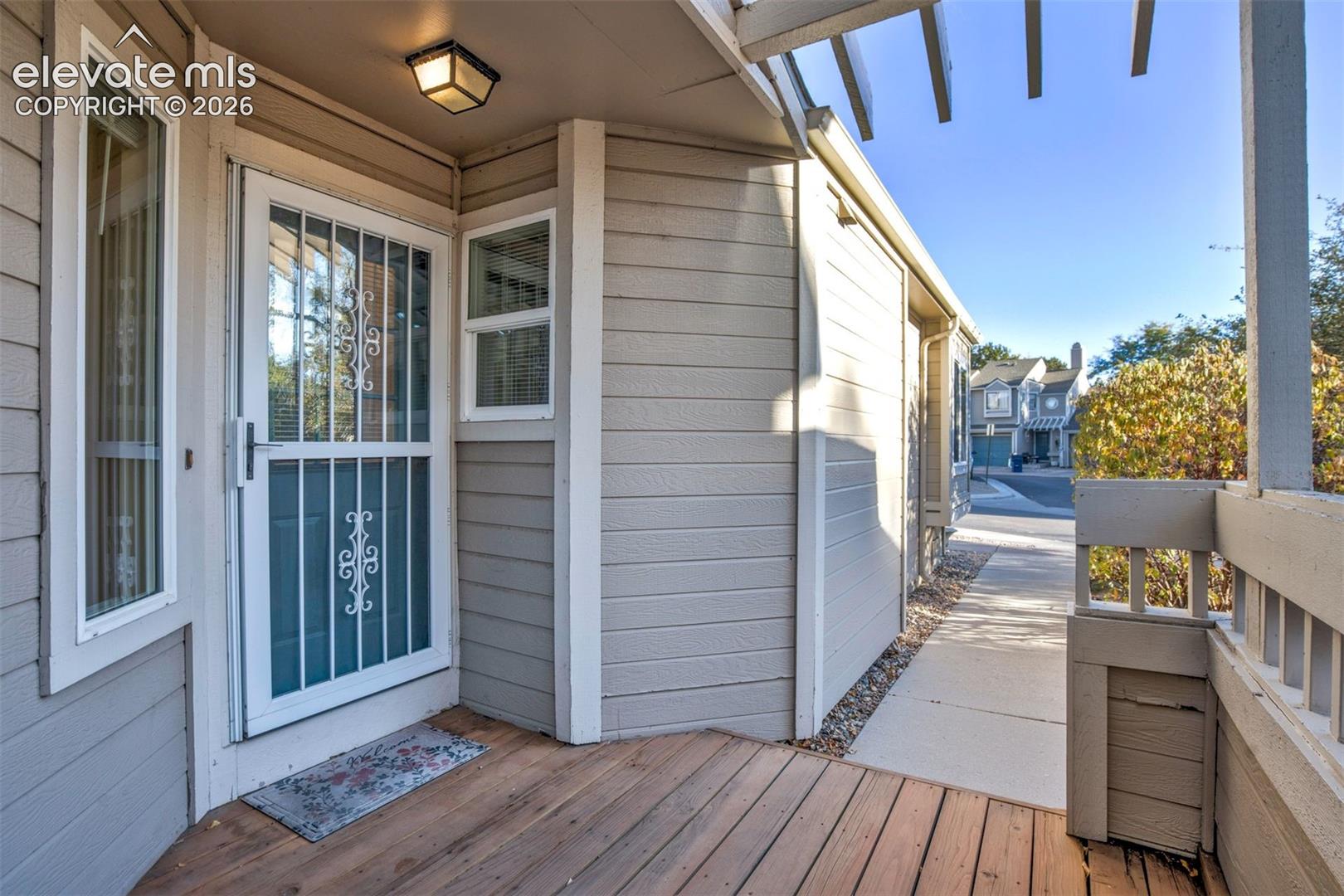 Covered porch featuring wood-finish decking, horizontal lap siding, a metal security screen door, and overhead pergola-style framing