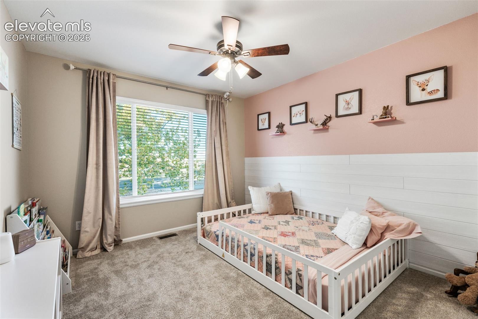 Horizontal plank wall treatment, large window with multi-pane configuration, neutral carpeting, and central ceiling fan with multi-light fixture