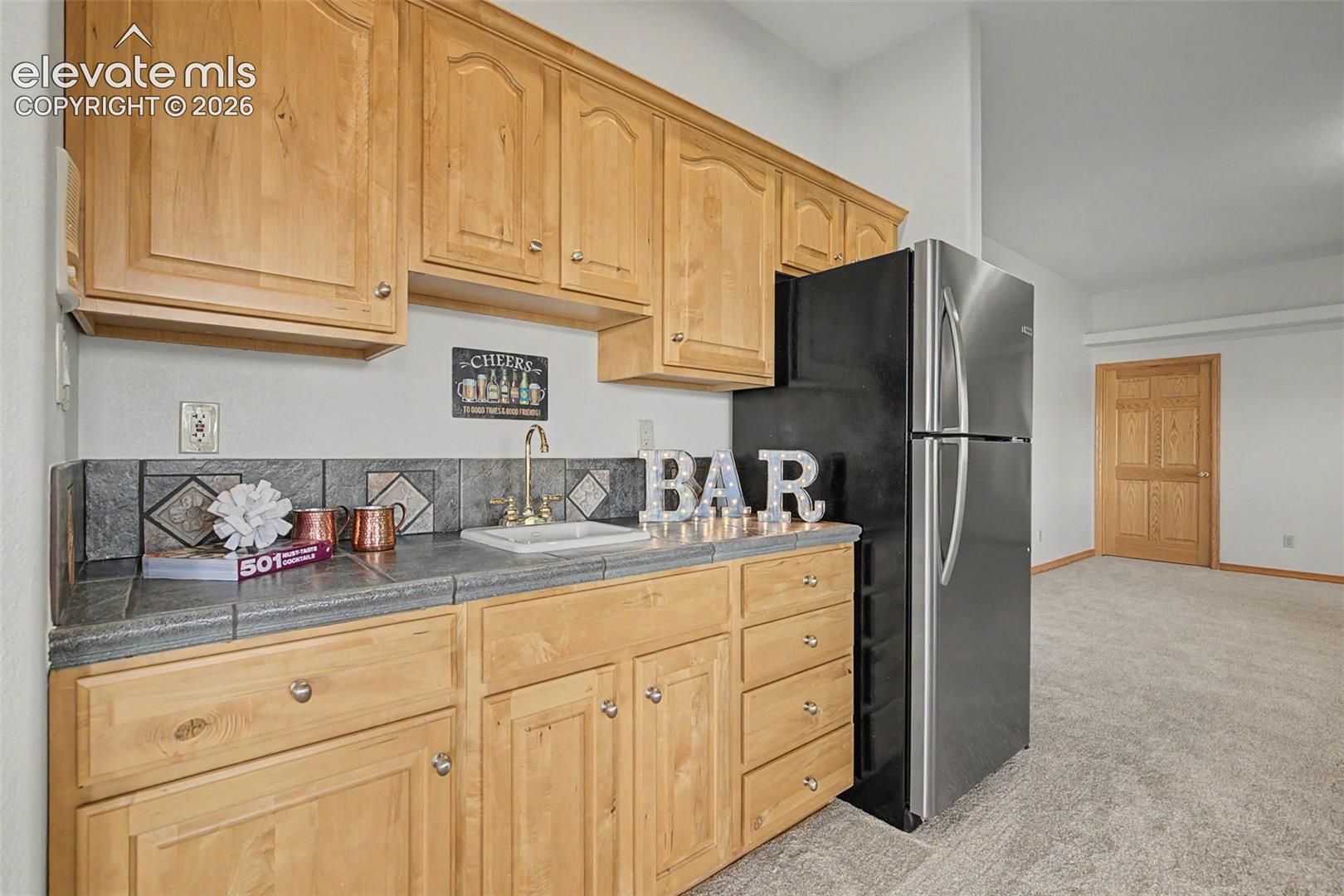 Wet bar featuring wood-finish cabinetry, tile countertop, and a stainless steel sink