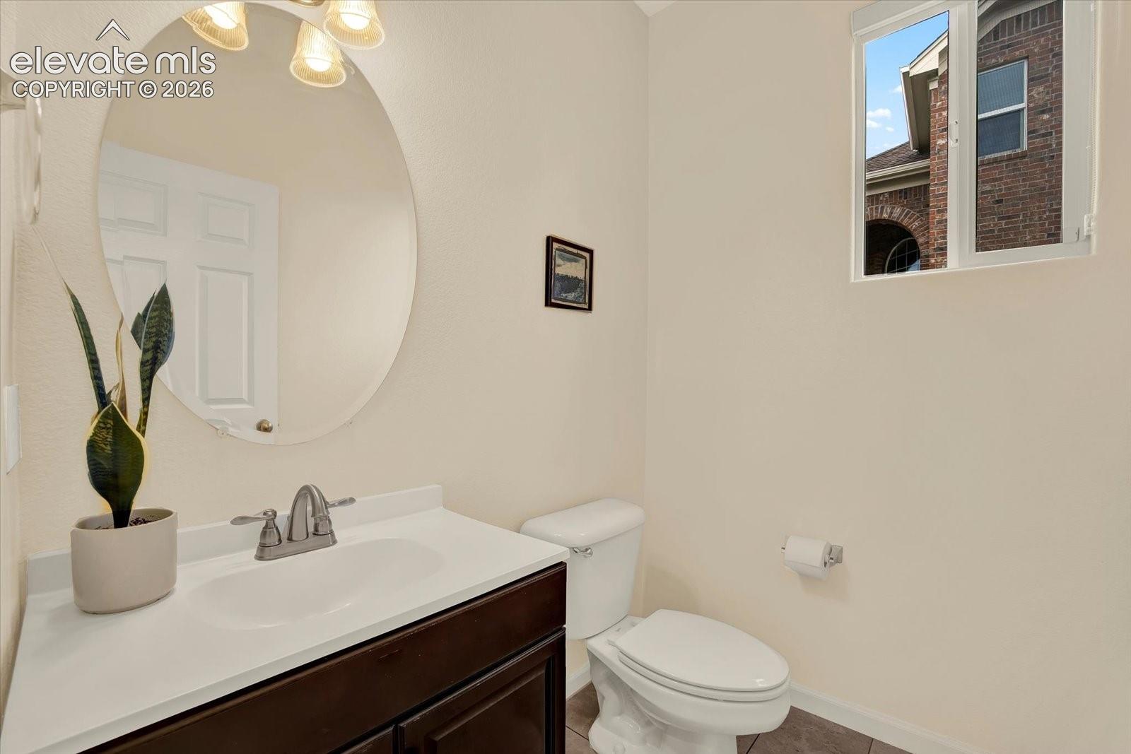 Dark wood-finish vanity with a white countertop and oval under-mount sink, large oval wall-mounted mirror, three-bulb integrated light fixture, and ceramic tile flooring