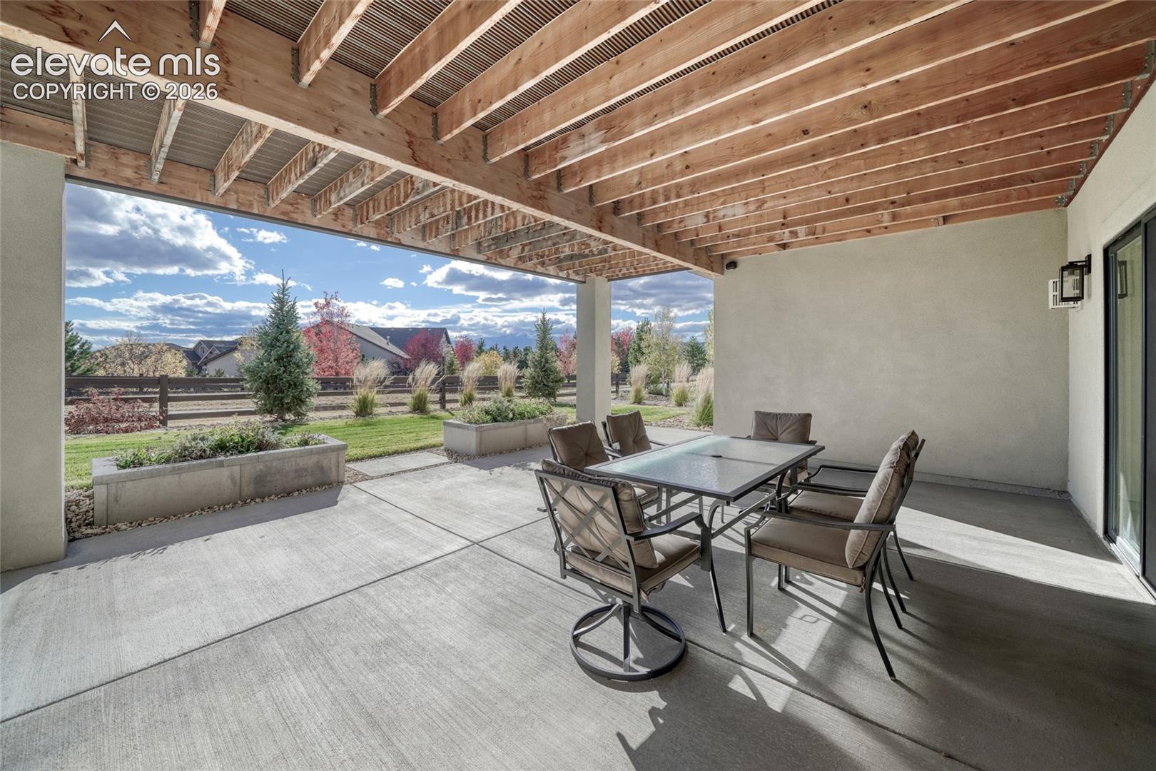 Covered patio featuring an exposed wood-beam ceiling, concrete flooring, and built-in masonry planters