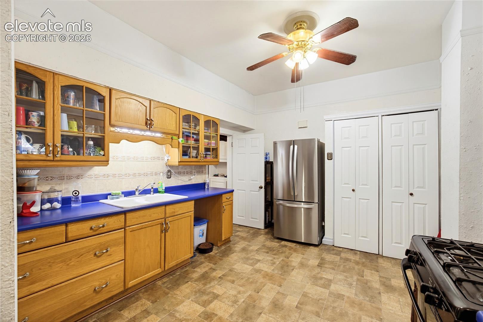 Full kitchen featuring wood-finish cabinetry with glass panel accents, a stainless steel French door refrigerator, and a ceiling fan light fixture