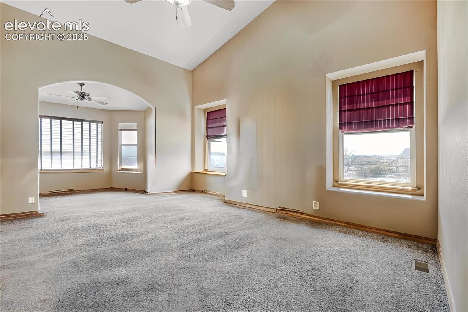 Spacious room featuring vaulted ceilings, light gray carpet, and an arched entryway