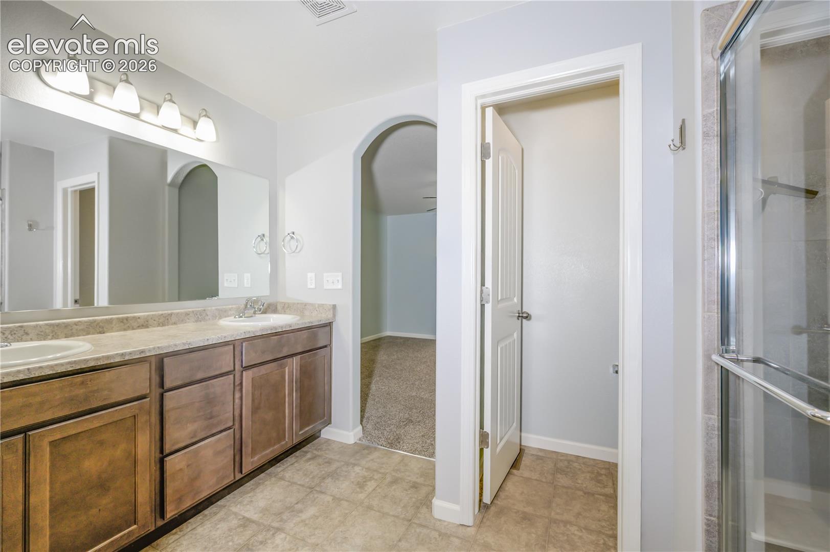 Dual vanity featuring stained wood cabinetry, stone-finish countertops, undermount sinks, and a full-width mirror with four-light fixture