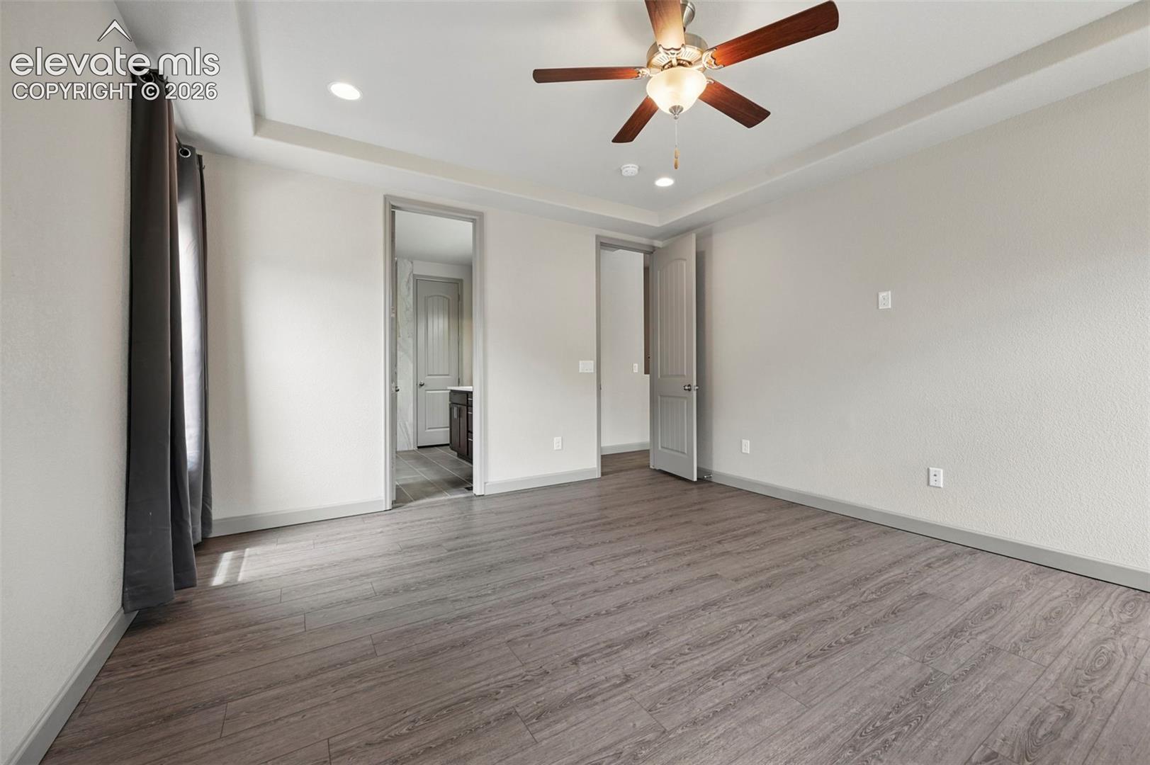 Tray ceiling, wood-finish flooring, ceiling fan with integrated light fixture, and recessed lighting