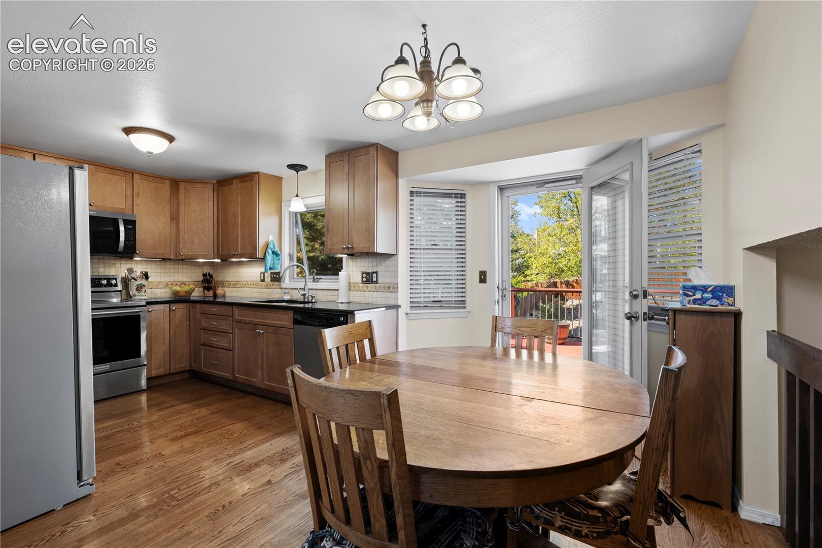 Kitchen featuring wood-finish cabinetry, stainless steel appliances, dark countertops, and a tiled backsplash