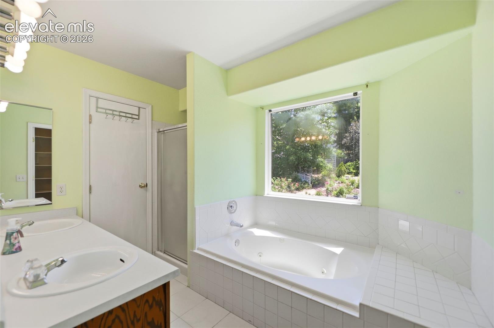 Bathroom featuring a large soaking tub with a tiled surround, a separate shower enclosure, and a dual-sink vanity with wood-finish cabinetry