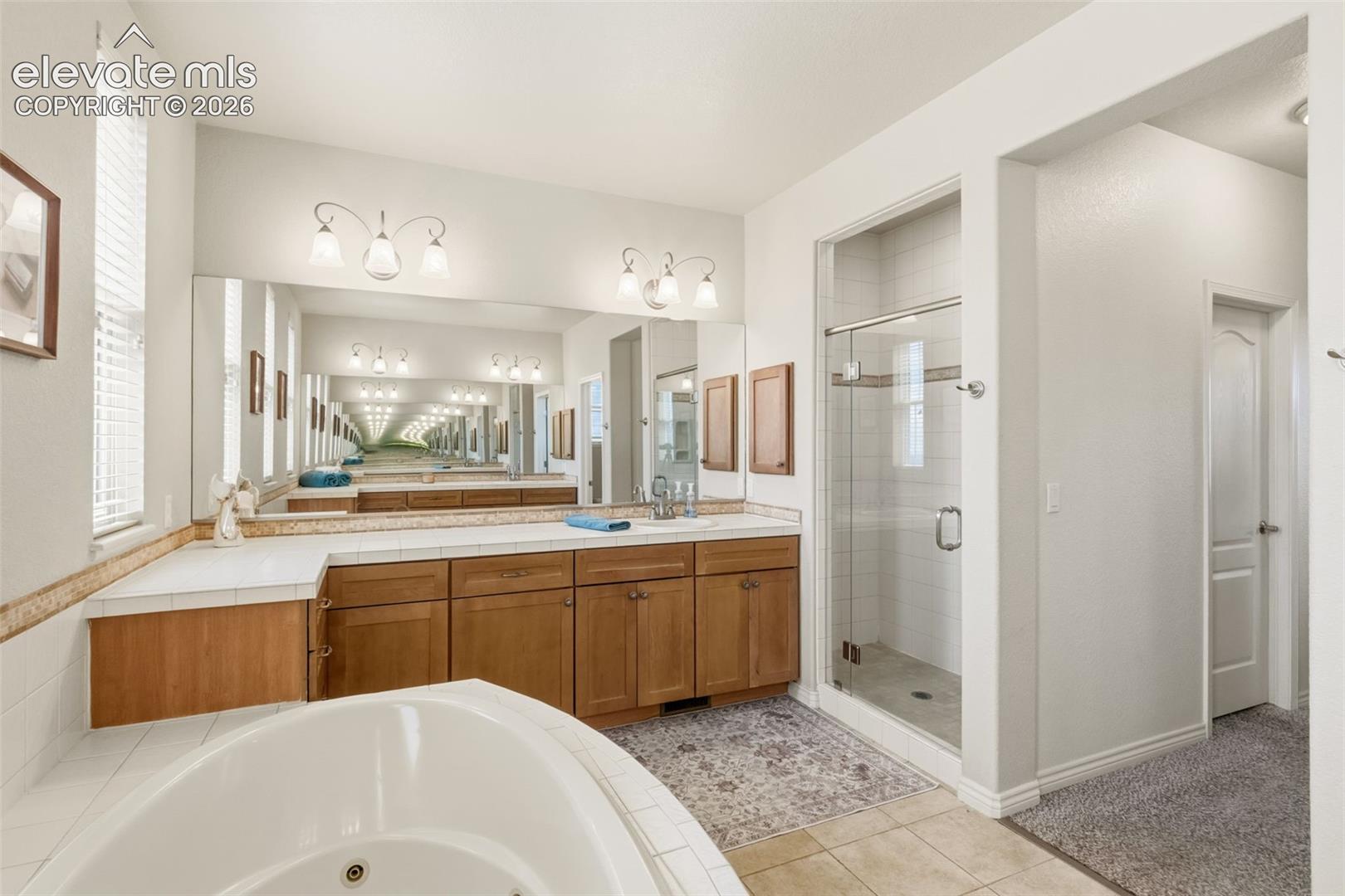 Bathroom featuring a dual vanity with wood cabinetry and a light-colored countertop, and a glass-enclosed shower