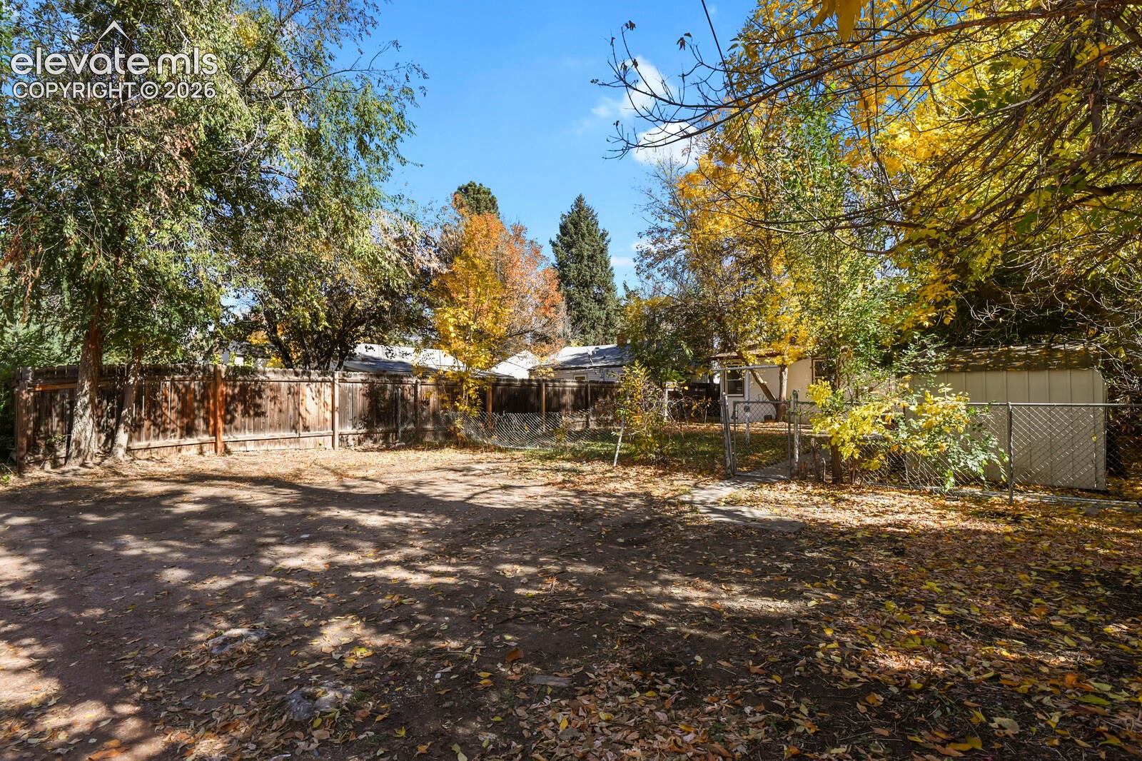 Expansive backyard featuring mature trees, privacy fence, a detached storage shed, and a chain-link enclosure