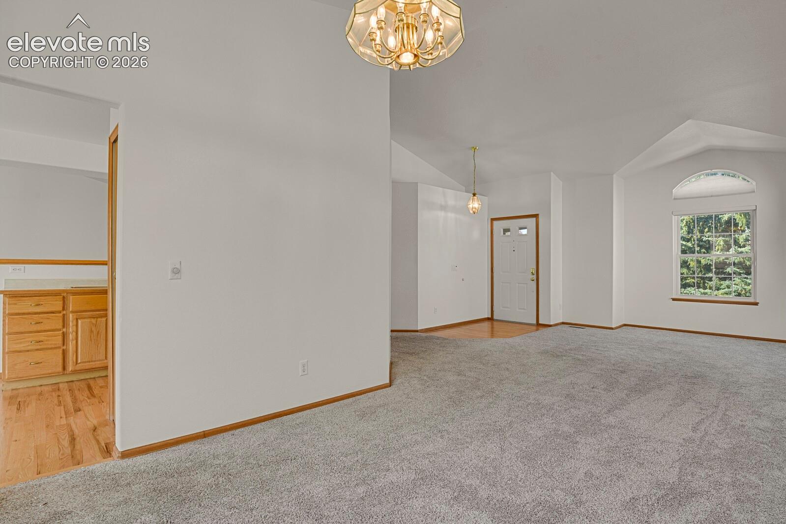 Vaulted ceiling, arched window, carpeted flooring, wood-finish flooring, and a decorative light fixture