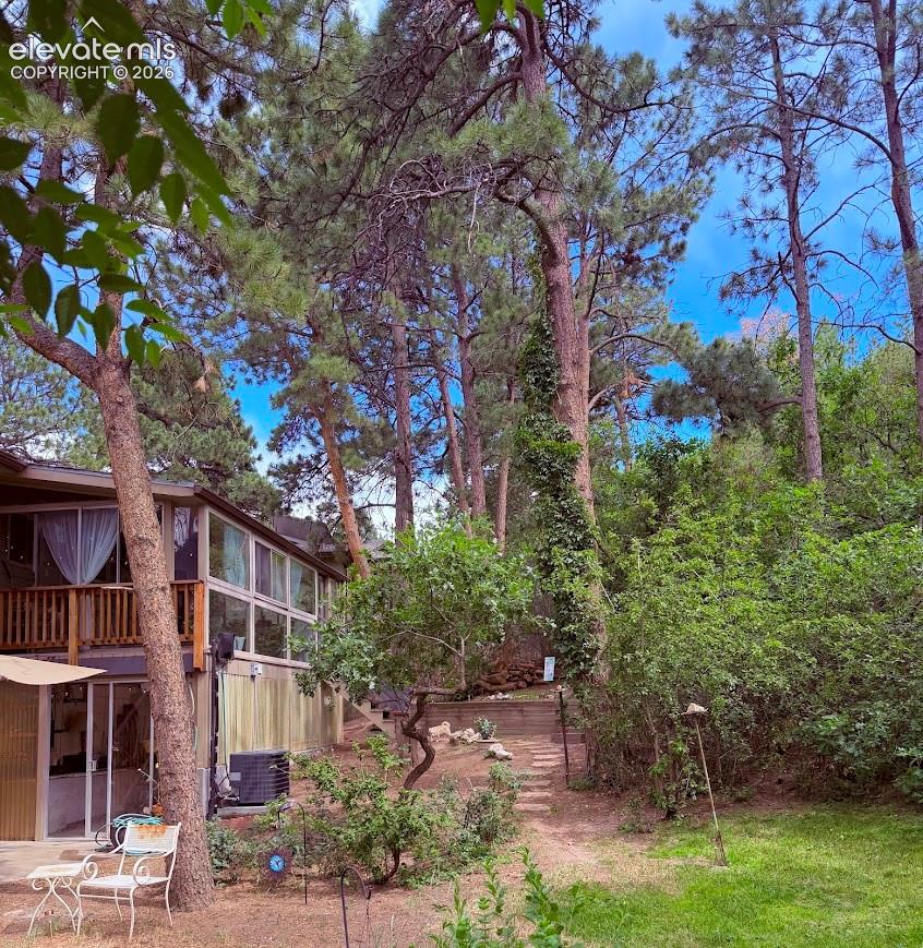 Elevated property featuring extensive natural landscaping with mature trees, a multi-level deck, ground-floor patio, and a tiered pathway