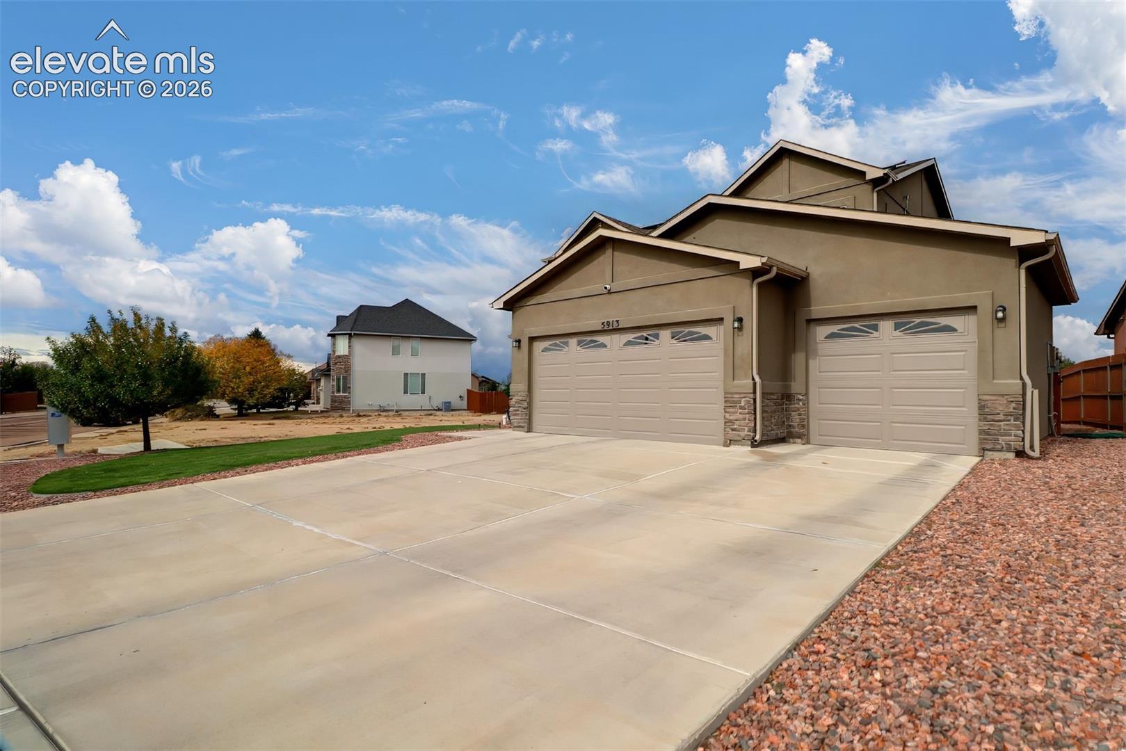 Multi-level exterior featuring a stucco facade, stone veneer accents, a three-car garage, and a concrete driveway